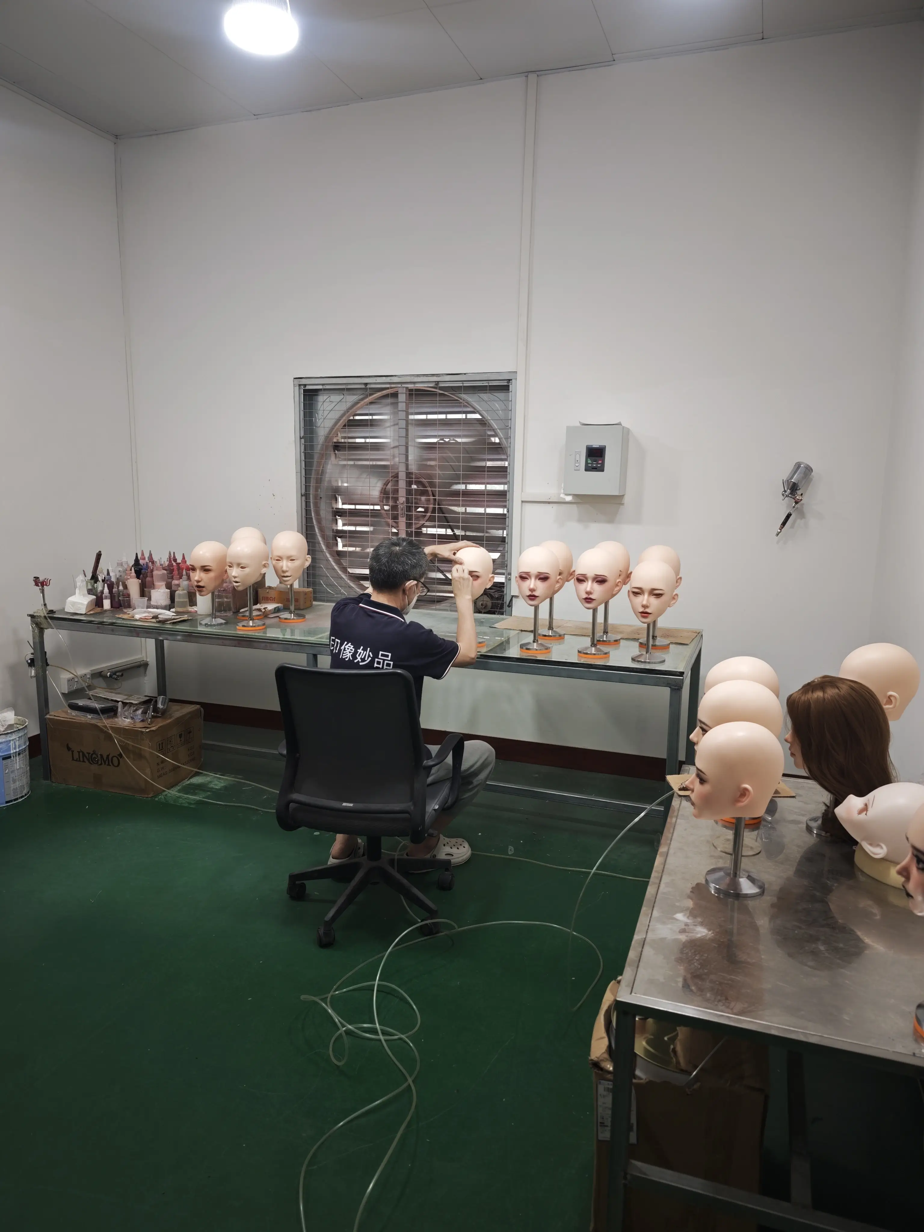 Production worker painting facial details on multiple artificial doll heads